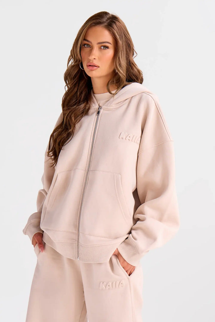 Woman wearing a beige hoodie and pants with branding on a white background