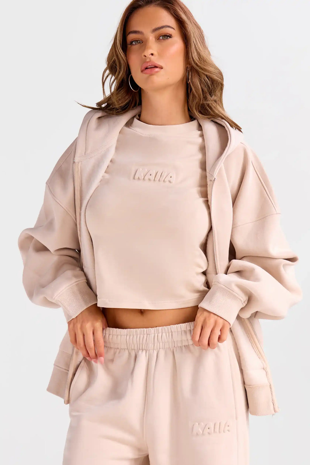 Woman wearing a beige tracksuit with 'Kuulua' branding on a white background