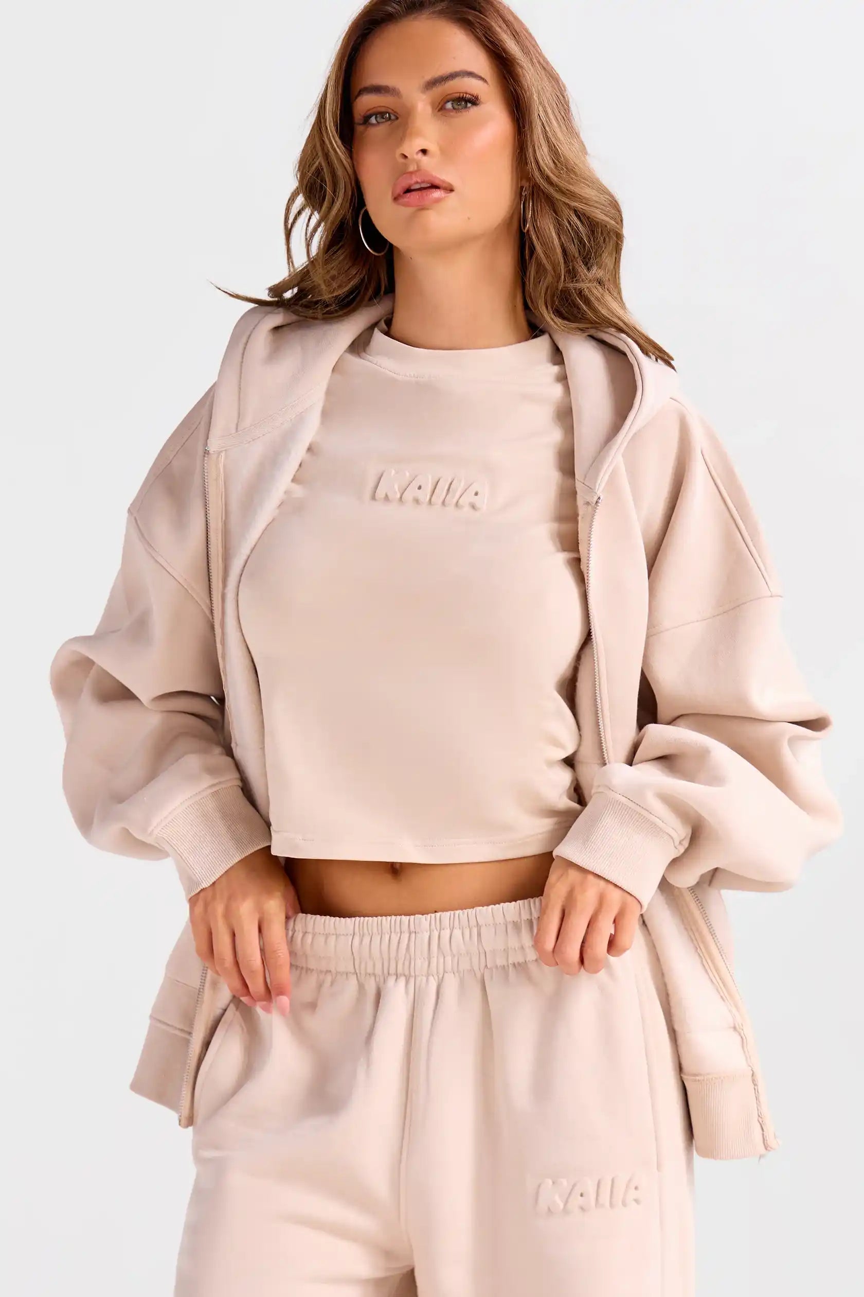 Woman wearing a beige tracksuit with 'Kuulua' branding on a white background